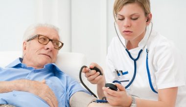 Young nurse checking the blood pressure of her old senior patient at hospital